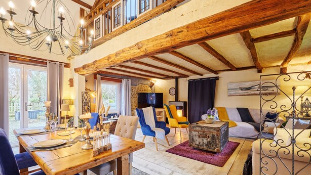 A rustic interior with exposed wooden beams, a stone fireplace, and a dining area with a wooden table and chairs. - Le Hamelinet by Interhome (Surville)