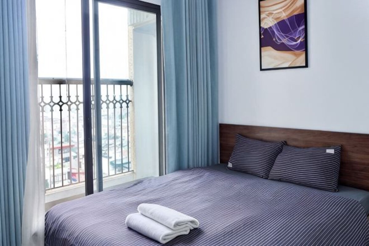 Una habitación de hotel con cama, ventana con cortinas, balcón y un cuadro en la pared.