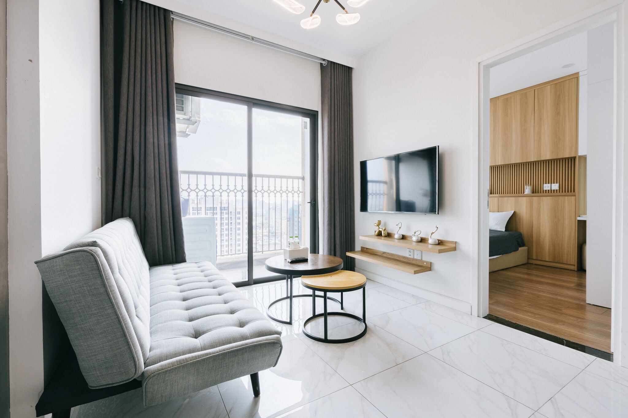 A modern living room with a grey sofa, a small round table, a TV mounted on the wall, and a wooden cabinet.