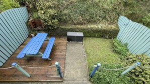 Un área de picnic con bancos y una mesa, rodeada por un bajo muro de piedra y follaje.