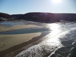 Une plage à l’eau claire, avec un rivage sablonneux, et une personne qui se promène.