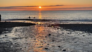 Una playa al atardecer, con el sol reflejándose en el agua.