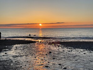 A beach at sunset with the sun reflecting on the water.