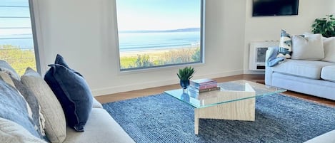 A living room with a large window, a white sofa, a glass coffee table, and a flat-screen TV.
