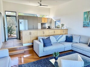A modern living room with a sofa and coffee table, a kitchen with wooden cabinets, and a dining area with a table and chairs.