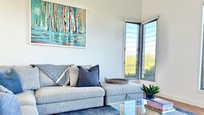 A modern living room with a sofa, a glass coffee table, a painting, and a view through a window. - Coastal Escape - Freycinet Holiday Houses (Coles Bay)