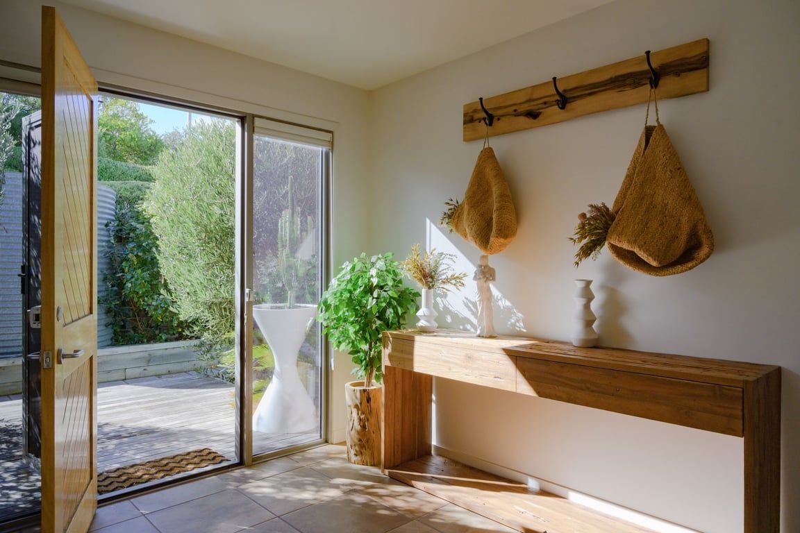 A room with a wooden bench, a white vase, and a hanging plant.