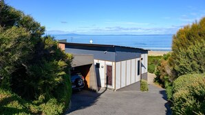 A modern building with a garage, a paved driveway, and a view of the ocean. - Coastal Escape - Freycinet Holiday Houses (Coles Bay)