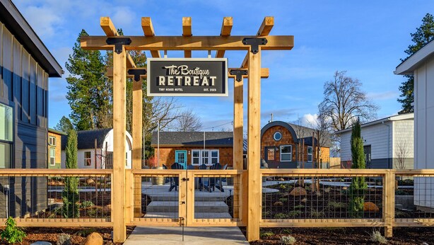 Een houten pergola leidt naar The Boutique Retreat bij Tiny House Hotel, met een helder uitzicht op de omliggende gebouwen en een verzorgde tuin.