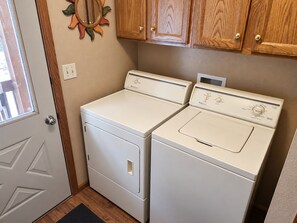A laundry room with two white front-loading washers and dryers, wooden cabinets above, and a window with a view.