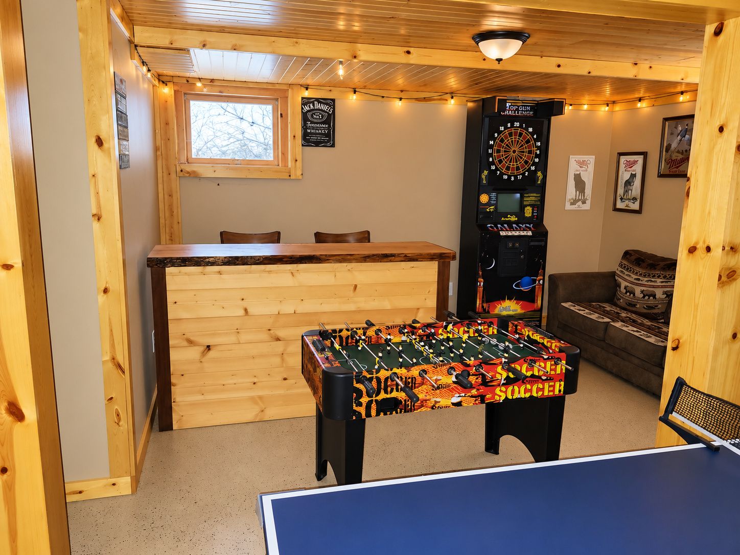 A room with a foosball table, dartboard, and a billiards table.