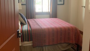 Un dormitorio con una cama, piso de madera, una ventana con cortinas y una lámpara en el techo.