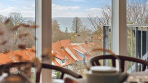 Blick durch ein Fenster auf einen klaren Himmel, ein Gewässer und Gebäude mit roten Dächern.