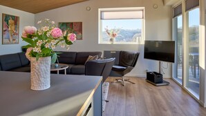 Ein modernes Wohnzimmer mit Holzboden, einem großen Fenster mit Blick, einem Flachbildfernseher und einem Sofa.