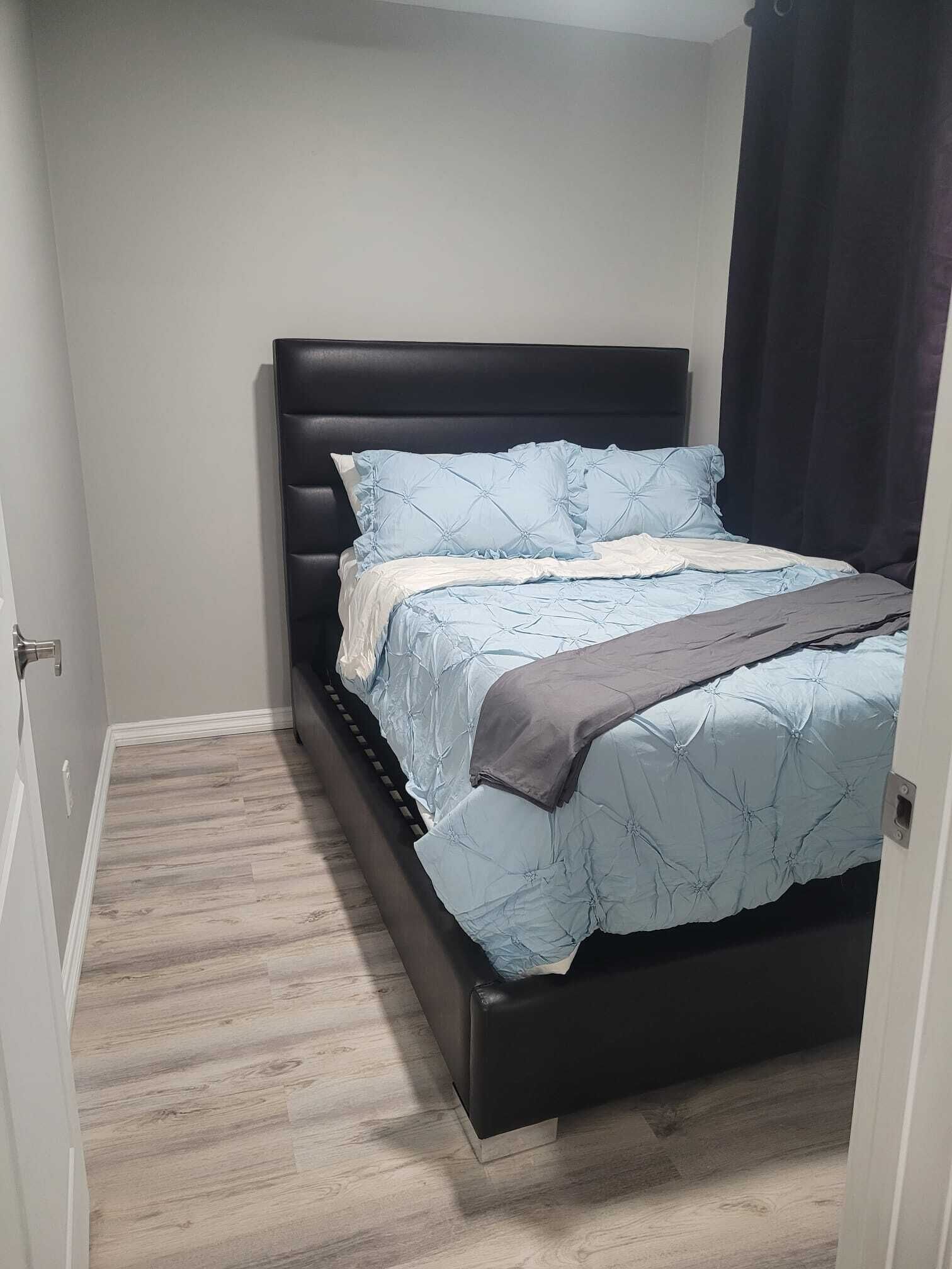 Un dormitorio con cabecera oscura, una cama con colcha azul claro y suelo de madera.