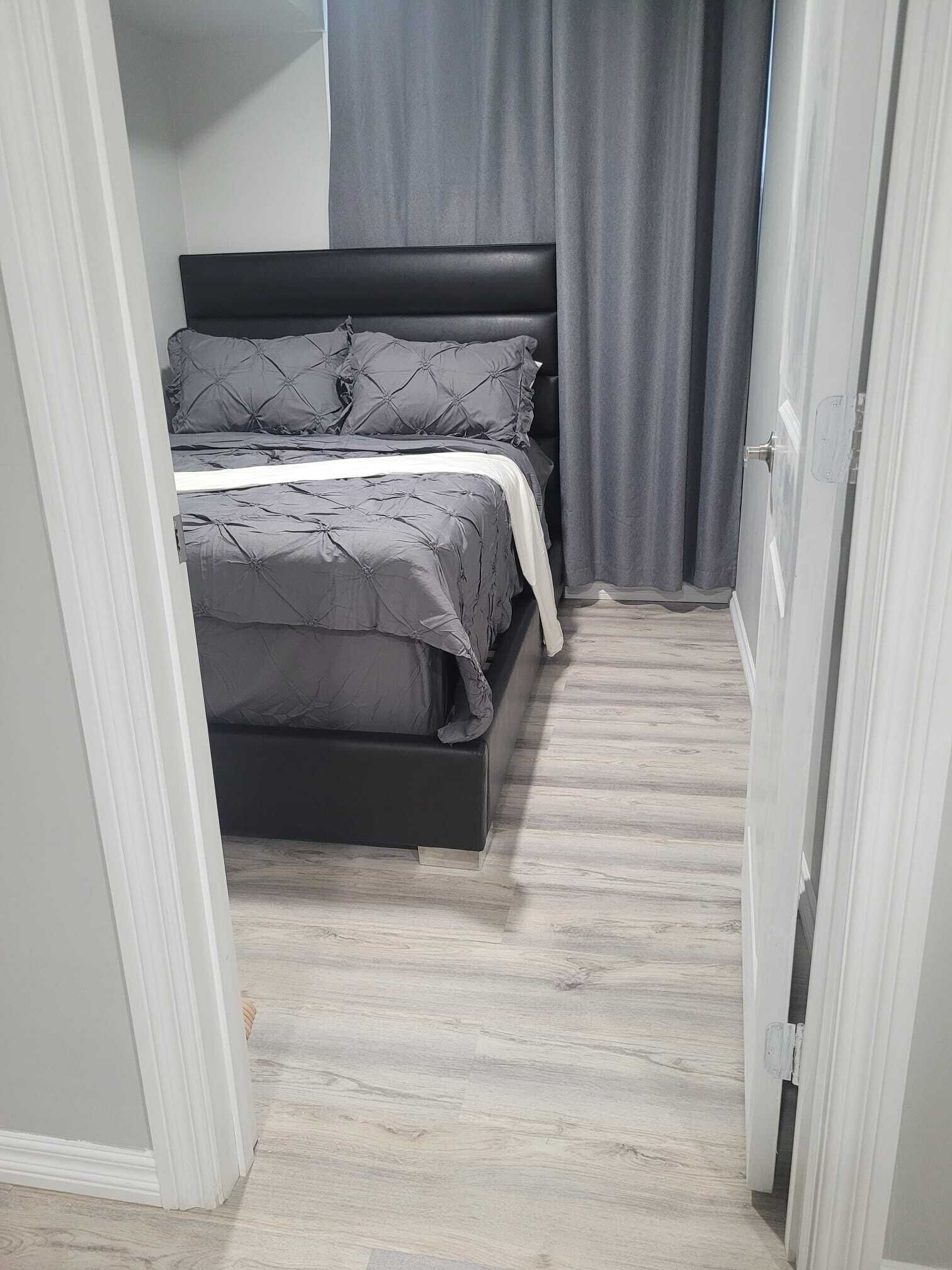 Une petite pièce avec un lit, des rideaux gris et une porte blanche.