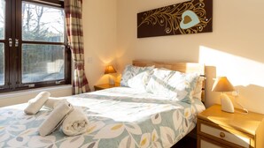 A neatly made bed with a floral bedspread, two bedside lamps, and a wall-mounted artwork. - Glenfiddich by Interhome (Aviemore)