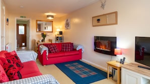 A cozy living room with a red sofa, a blue checkered sofa, a fireplace, a TV, and a small table with a lamp. - Glenfiddich by Interhome (Aviemore)