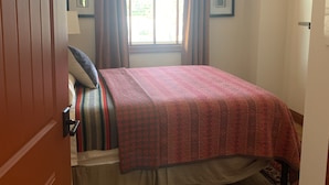 Un dormitorio con una cama, piso de madera, una ventana con cortinas y una lámpara en el techo.