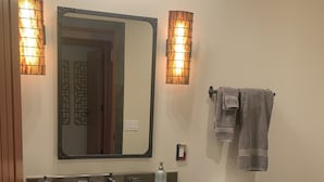 Un baño con lavamanos, espejo, dos luces empotradas, inodoro y un perchero para toallas.