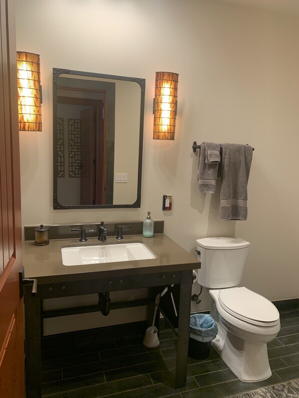 Un baño con lavamanos, espejo, dos luces empotradas, inodoro y un perchero para toallas.