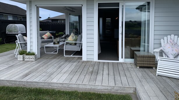 Une terrasse couverte avec des sièges d’extérieur, un barbecue et une porte-fenêtre coulissante donnant sur un espace intérieur.