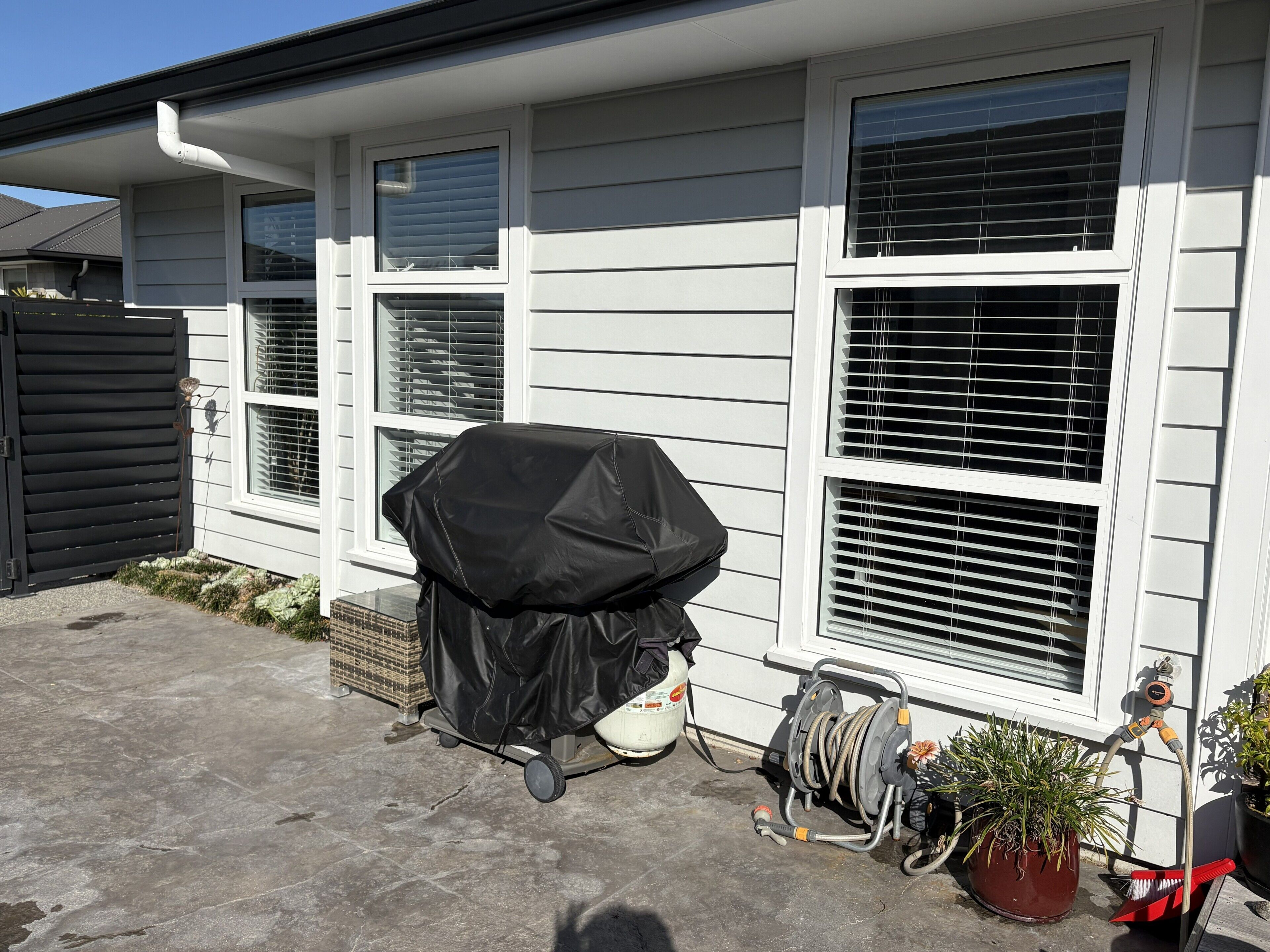A house with a covered grill, a hose reel, and a potted plant.