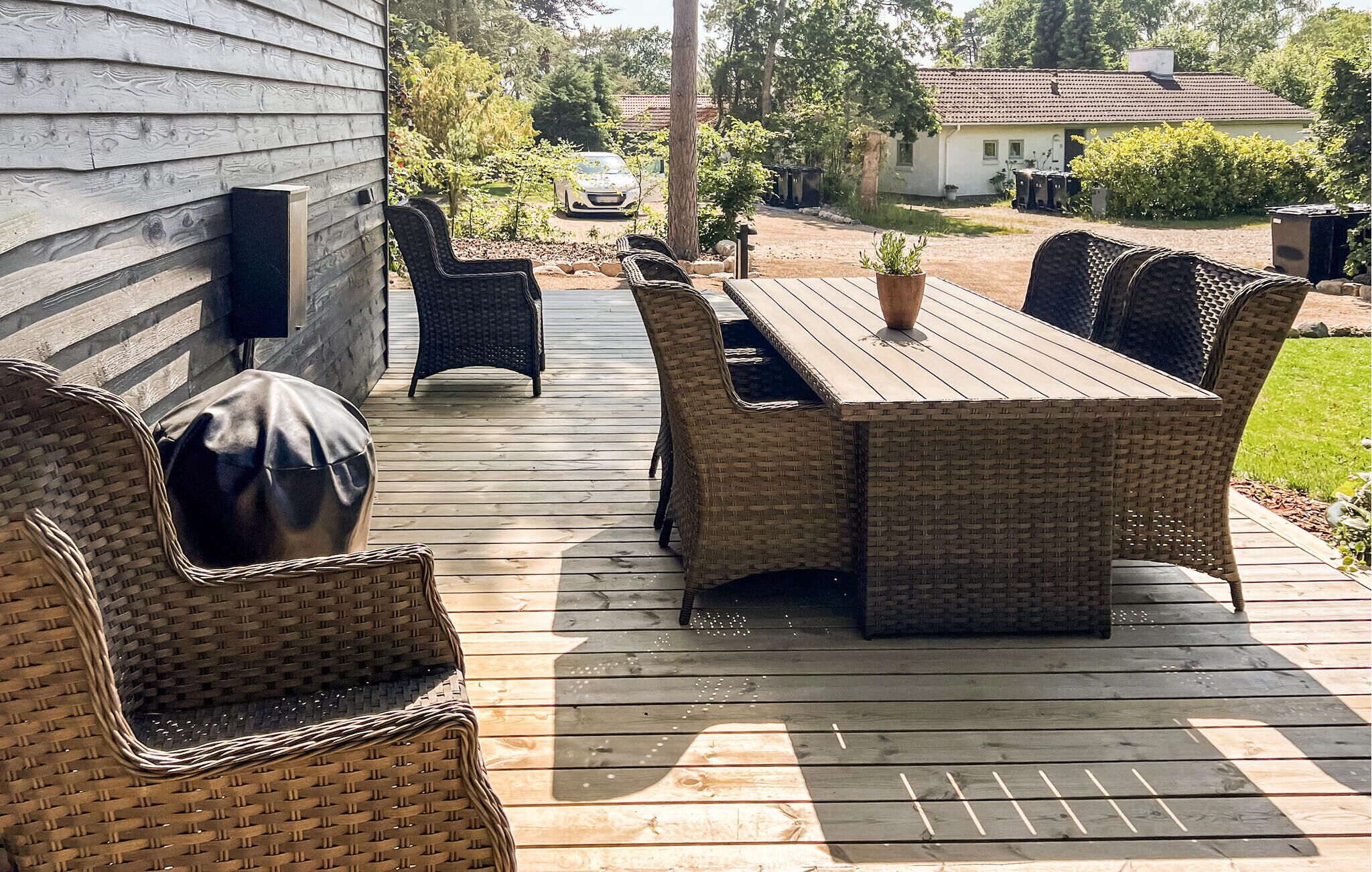 An outdoor patio with wicker furniture, a wooden table, and a potted plant.