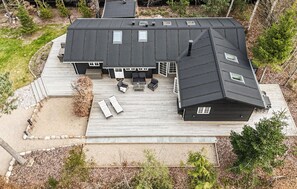 Une maison moderne dotée d’une grande terrasse, de nombreuses fenêtres et d’une cheminée.