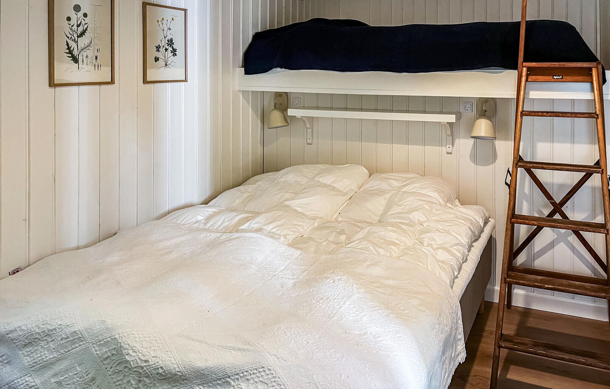 Een eenpersoonsbed met een witte deken, een houten ladder en twee wandlampen.