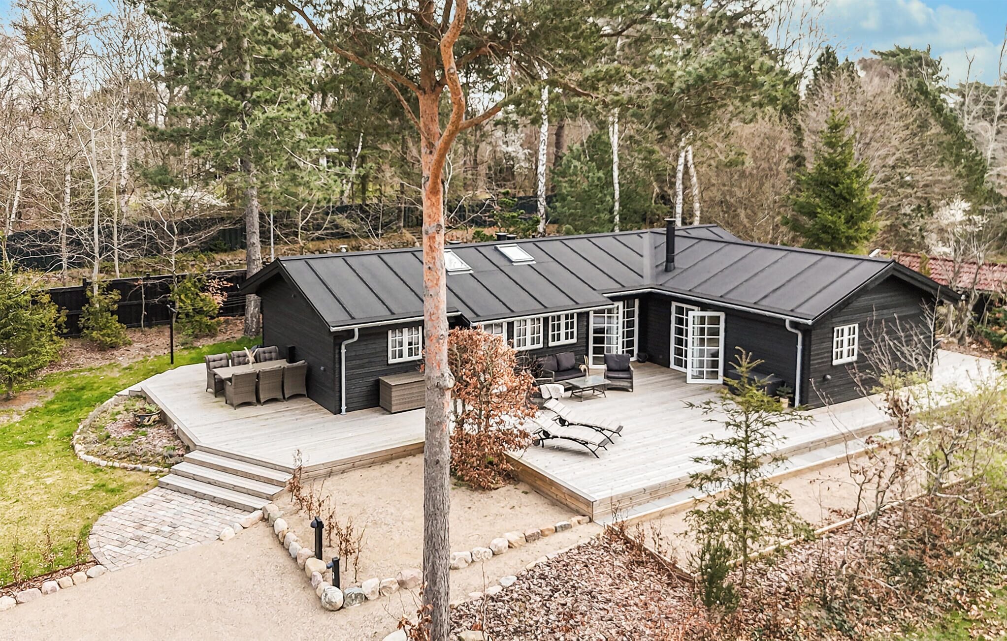A black house with a large deck, surrounded by trees.