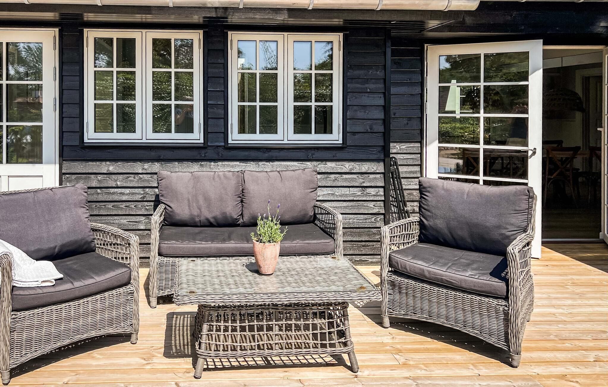 A wooden deck with a sofa and two chairs, a small table, and a potted plant.