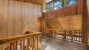 Interior de madera con una escalera, barandillas de madera y una ventana con vistas a árboles.