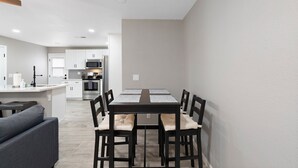 A modern kitchen with white cabinets, a central island, and a dining area with a table and chairs. - Papago Polka (Scottsdale)