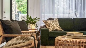 Una sala de estar con un sofá verde, sillas de mimbre, una mesita redonda y una planta en maceta.