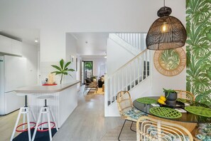 Ett modernt kök med en vit bänkskiva, två barstolar och en hängande lampa.