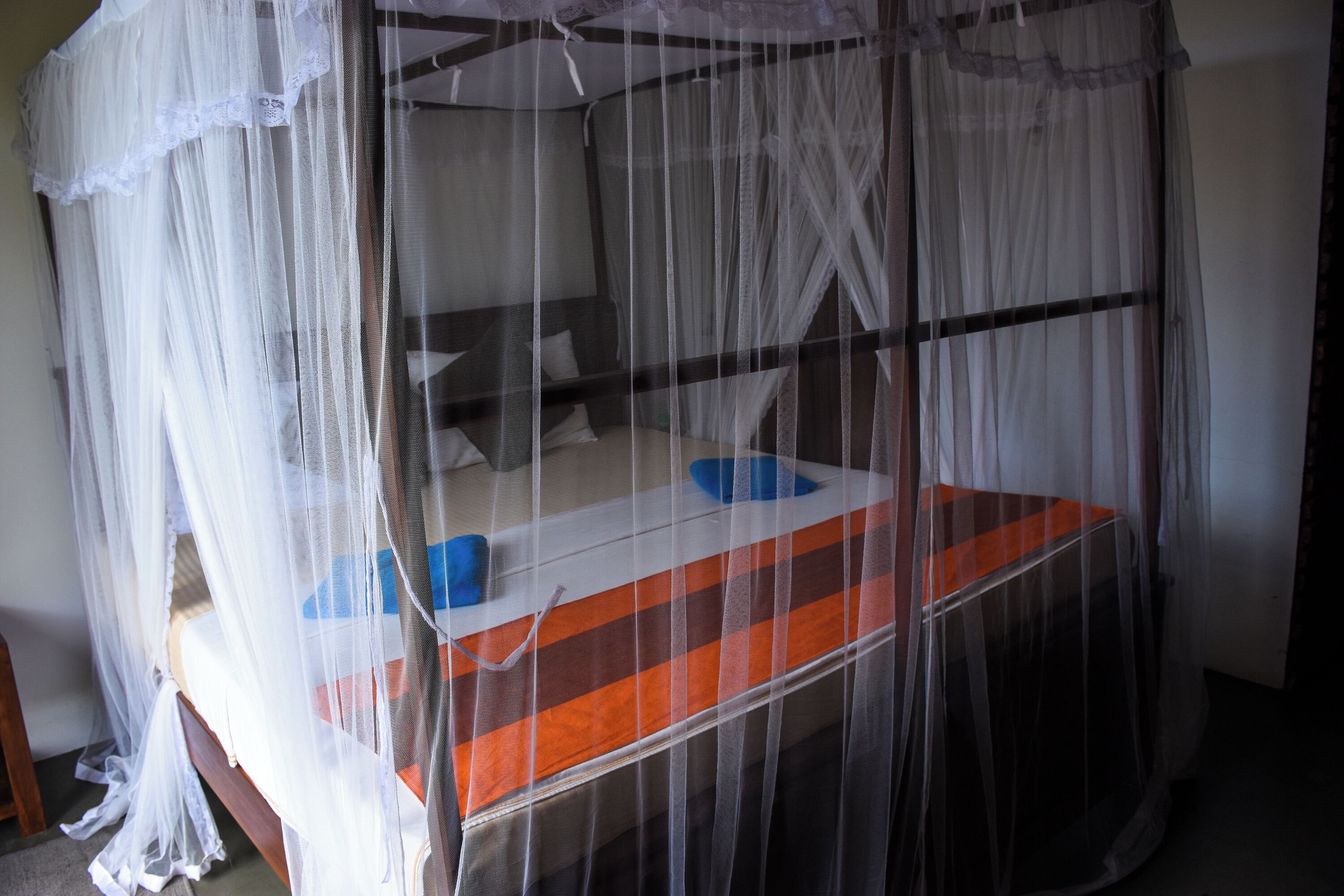 A bed with a mosquito net, a wooden headboard, and a striped mattress cover.