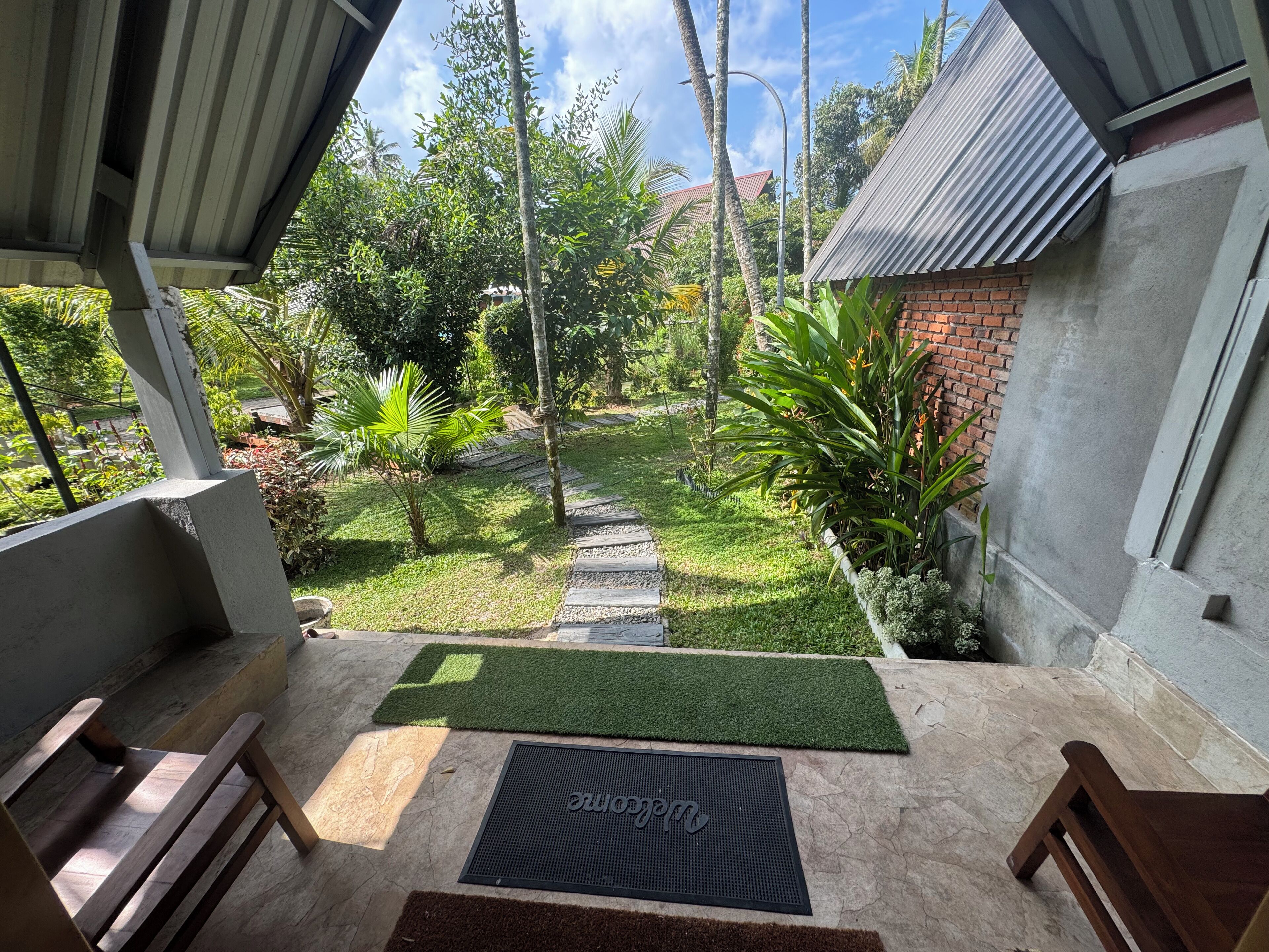 Un espace extérieur abrité, doté d’un sol en béton, d’un petit jardin avec un sentier et d’un banc.