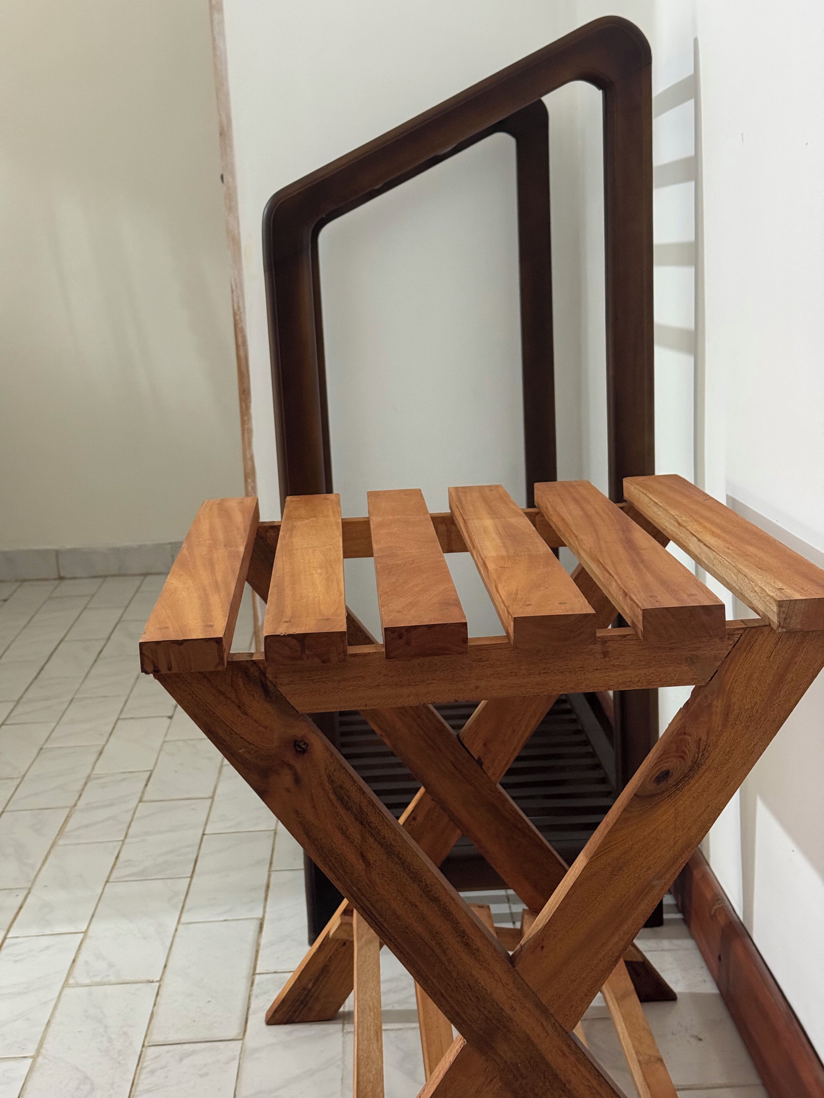 A wooden chair with a unique X-shaped frame design, placed in a room with tiled flooring and white walls.