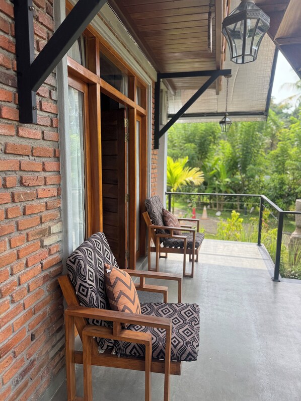 A wooden bench with patterned cushions on a balcony with a brick wall and a wooden door. - Steps Garden Resort (Miriswatte)