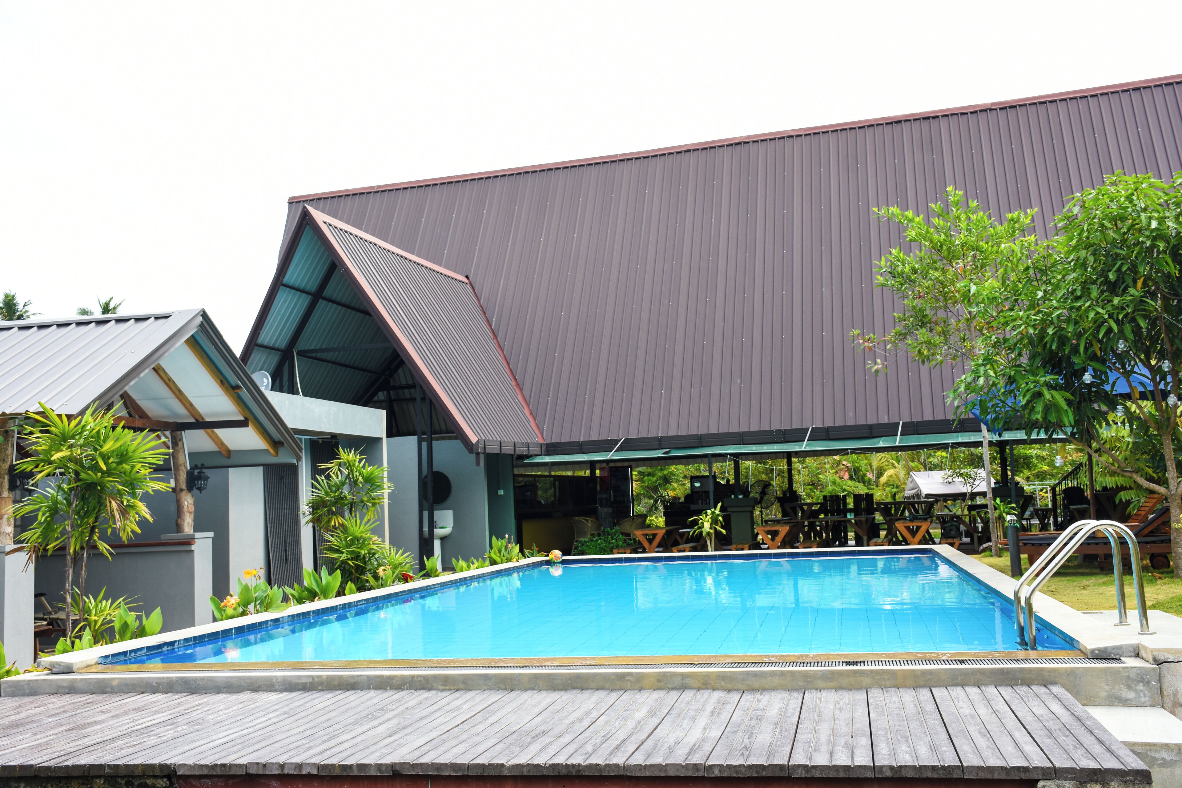 A swimming pool with a wooden deck, surrounded by outdoor seating and greenery.