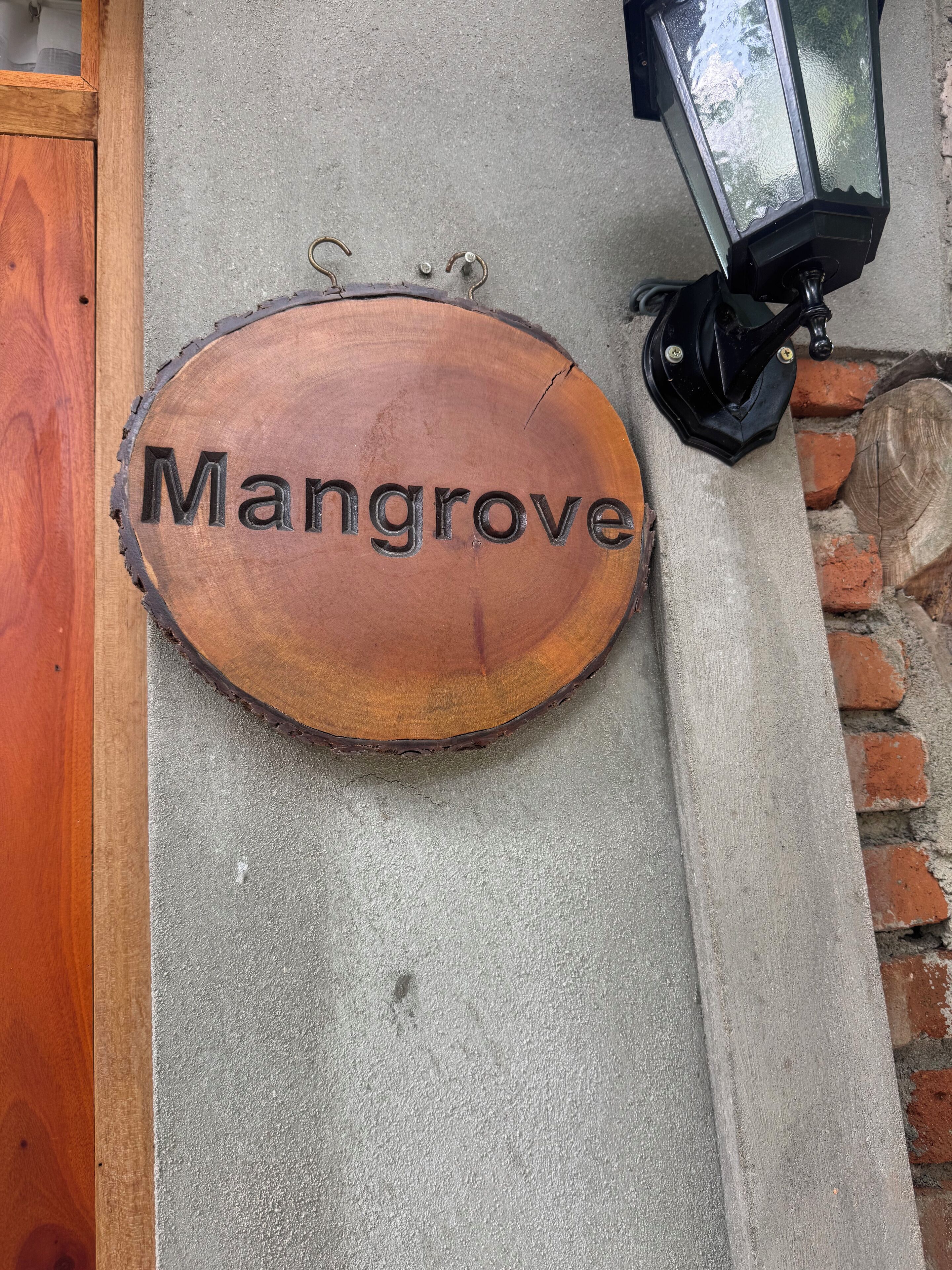 A wooden sign with the word 'Mangrove' mounted on a concrete wall.