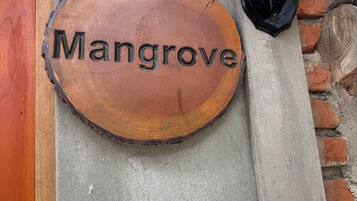 A wooden sign with the word 'Mangrove' mounted on a concrete wall.