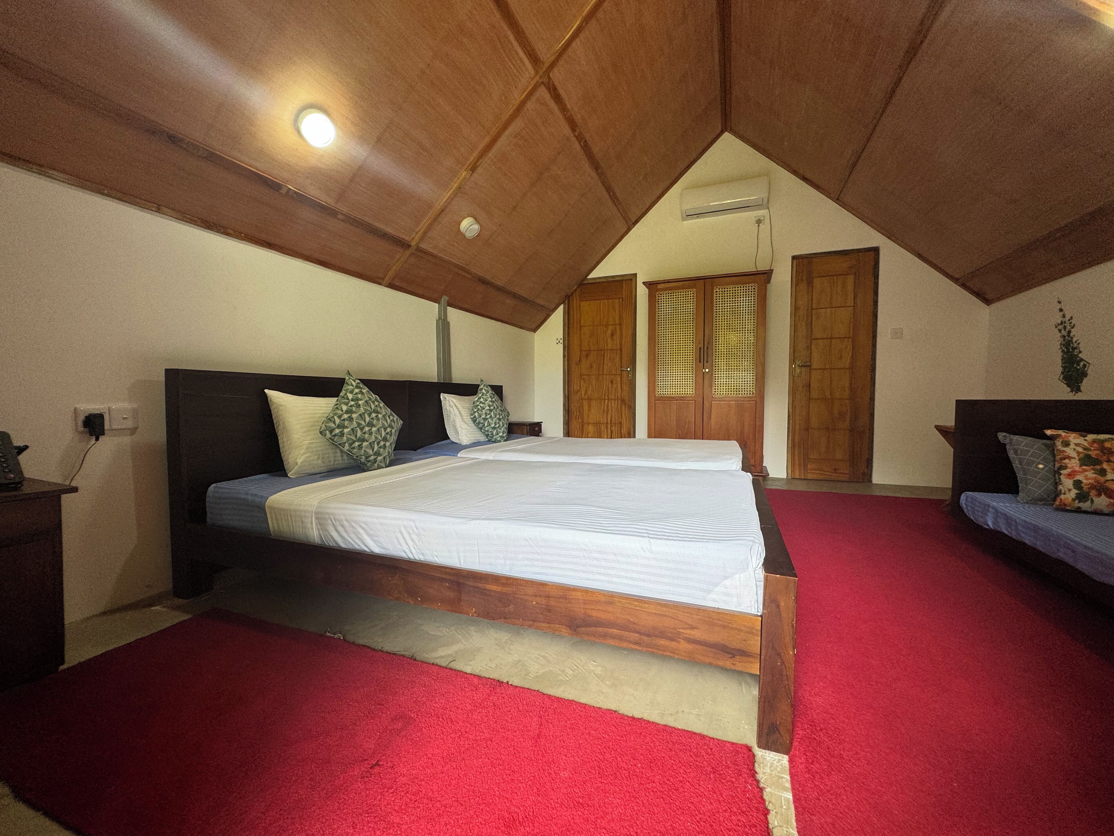Quarto com uma cama grande, uma cama menor, armários de madeira e um tapete vermelho.