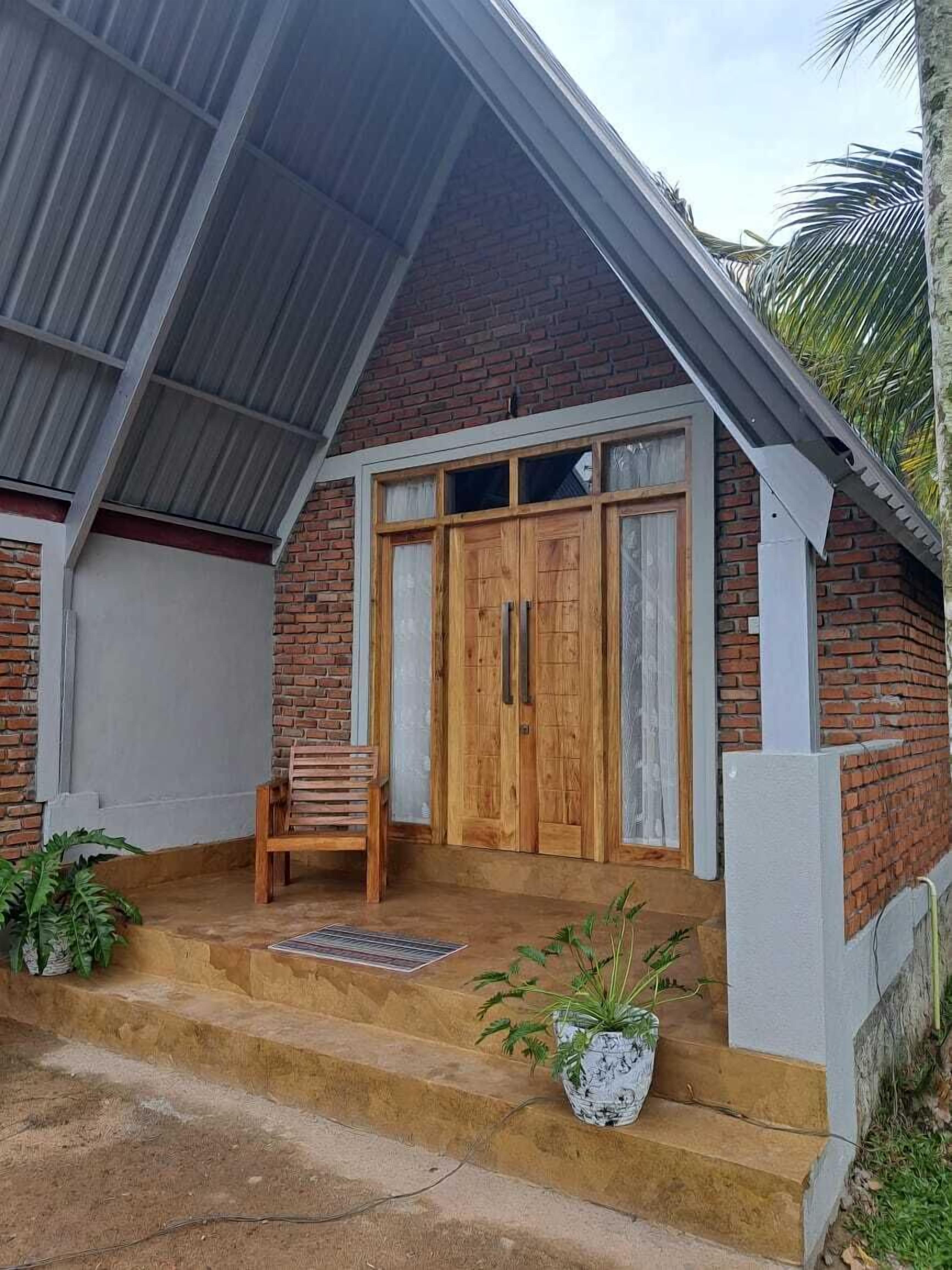 Una casa de dos pisos con fachada de ladrillo, puerta principal de madera y un pequeño porche con escalones que llevan a la entrada.