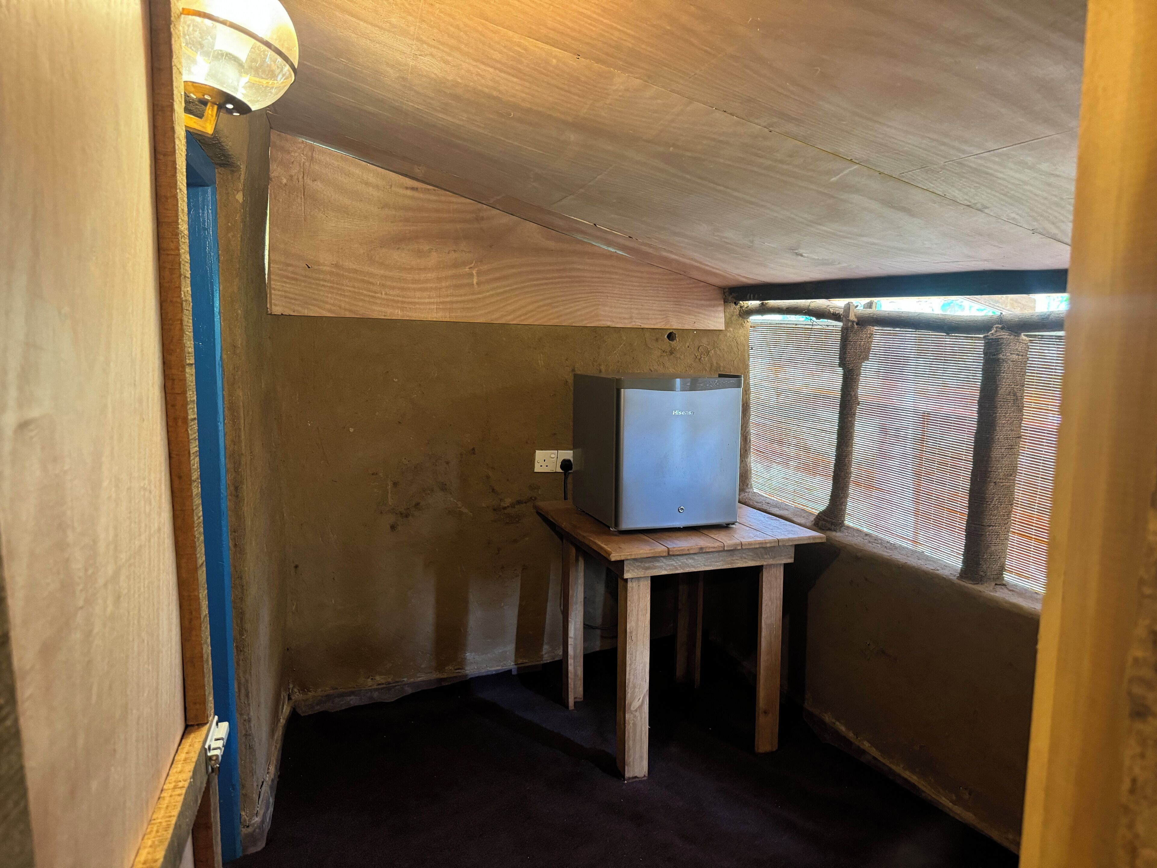 Una habitación pequeña y tenuemente iluminada, con techo de madera, una sola mesa y un televisor sobre un soporte.