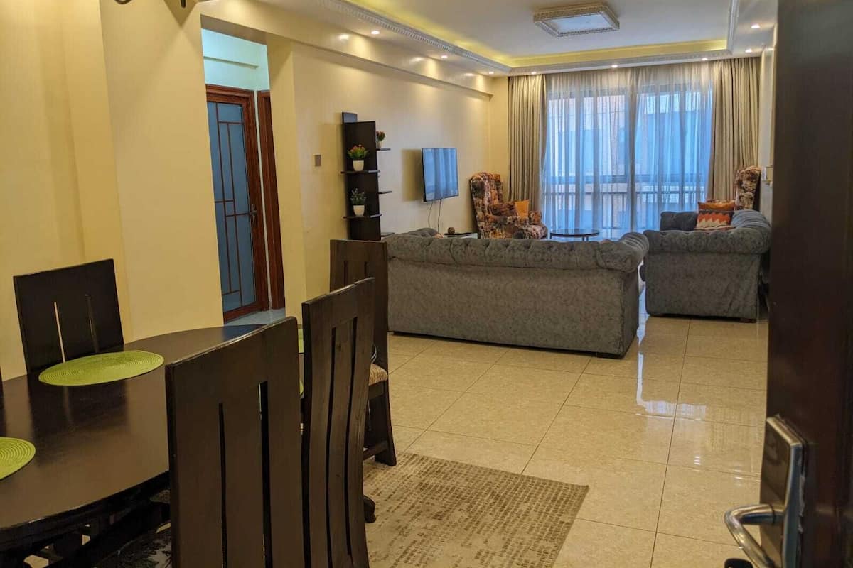Un salón amplio con un conjunto de sofás, una zona de comedor con mesa y sillas, y un televisor en la pared.