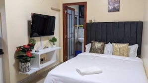 Een hotelkamer met een bed, een aan de muur bevestigde televisie, een klein plankje met decoratieve objecten en een deur naar een badkamer.