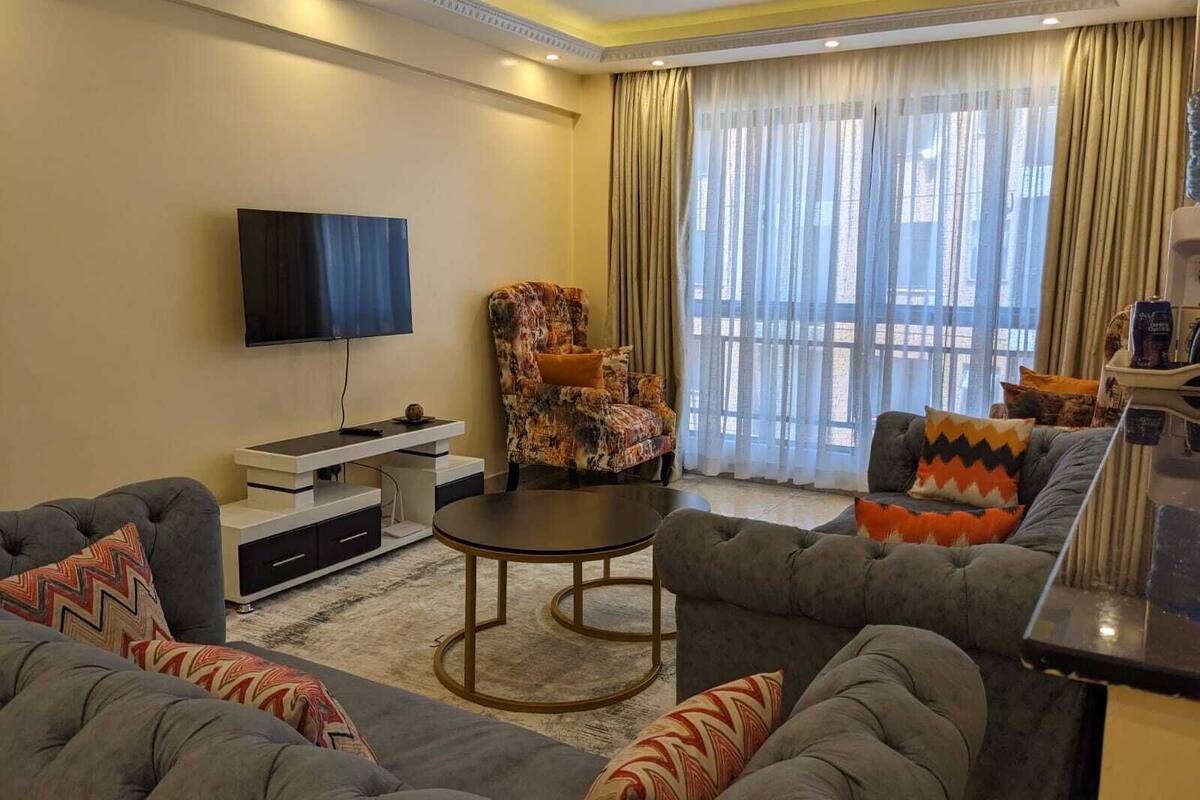 Una sala de estar moderna con un televisor de pantalla plana, un sillón estampado, un juego de sofá gris y una mesa de centro redonda.