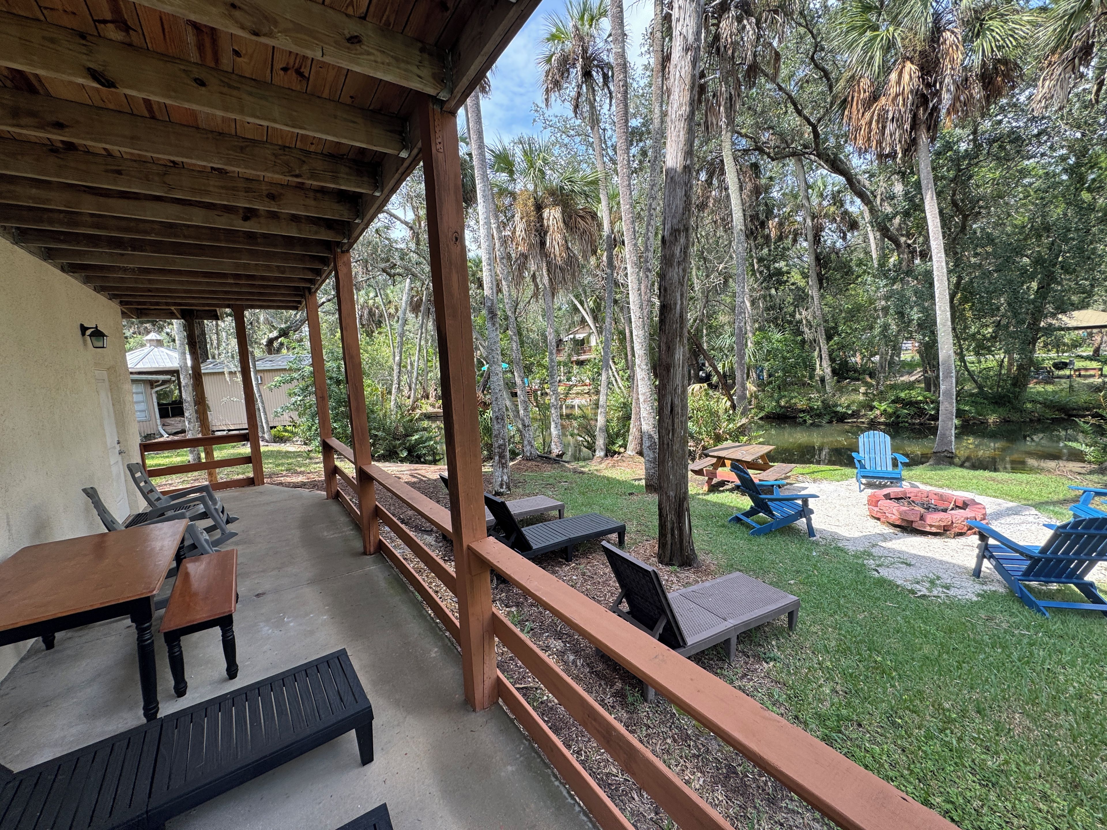 A covered outdoor area with wooden furniture, a fire pit, and a pond.